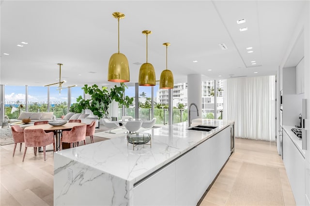 kitchen with light stone countertops, a kitchen island with sink, sink, and hanging light fixtures