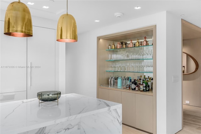 bar with light stone countertops, decorative light fixtures, and light wood-type flooring