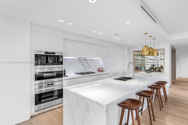 kitchen featuring white cabinets, pendant lighting, light hardwood / wood-style flooring, and a kitchen island with sink