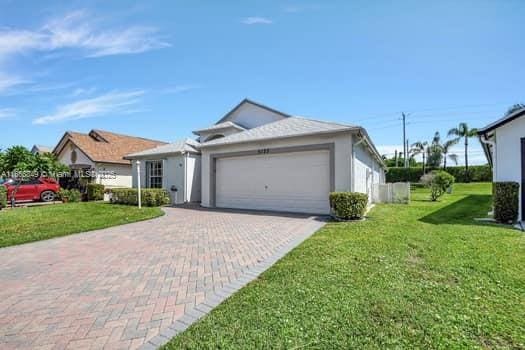 ranch-style house with a front yard, stucco siding, decorative driveway, and an attached garage