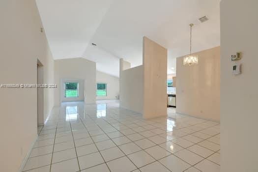 tiled empty room with lofted ceiling and a chandelier