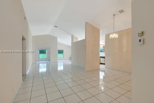 empty room featuring lofted ceiling, light tile patterned floors, and an inviting chandelier