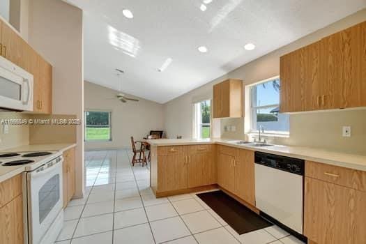 kitchen with a sink, white appliances, a peninsula, vaulted ceiling, and light countertops