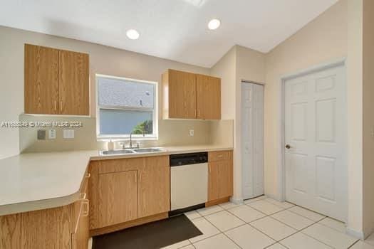 kitchen featuring sink, white dishwasher, vaulted ceiling, and light tile patterned floors