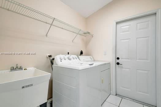 laundry area with light tile patterned flooring, independent washer and dryer, laundry area, and a sink