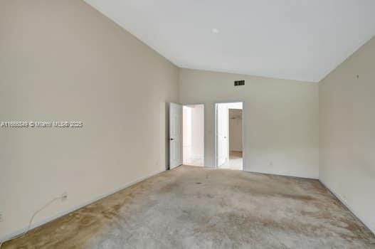 carpeted empty room featuring visible vents and vaulted ceiling