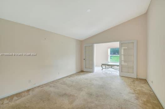 unfurnished room featuring french doors, light colored carpet, and vaulted ceiling