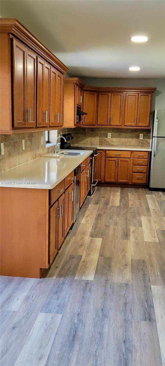 kitchen featuring backsplash, ventilation hood, sink, light hardwood / wood-style flooring, and stainless steel appliances