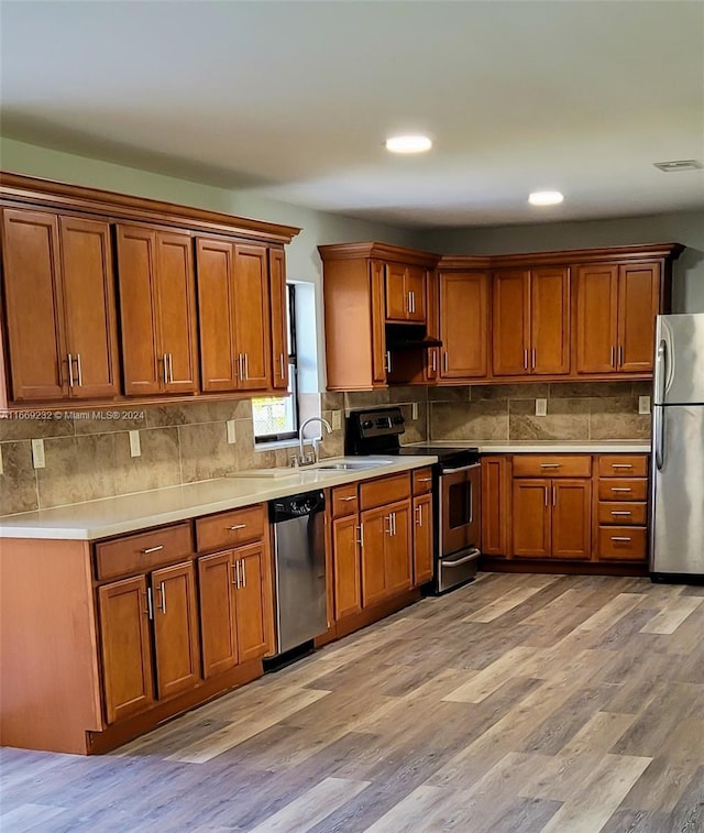 kitchen featuring decorative backsplash, stainless steel appliances, light hardwood / wood-style flooring, and sink