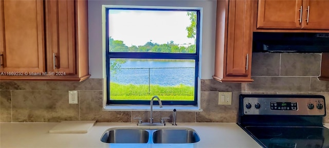 kitchen featuring stove, tasteful backsplash, exhaust hood, sink, and a water view