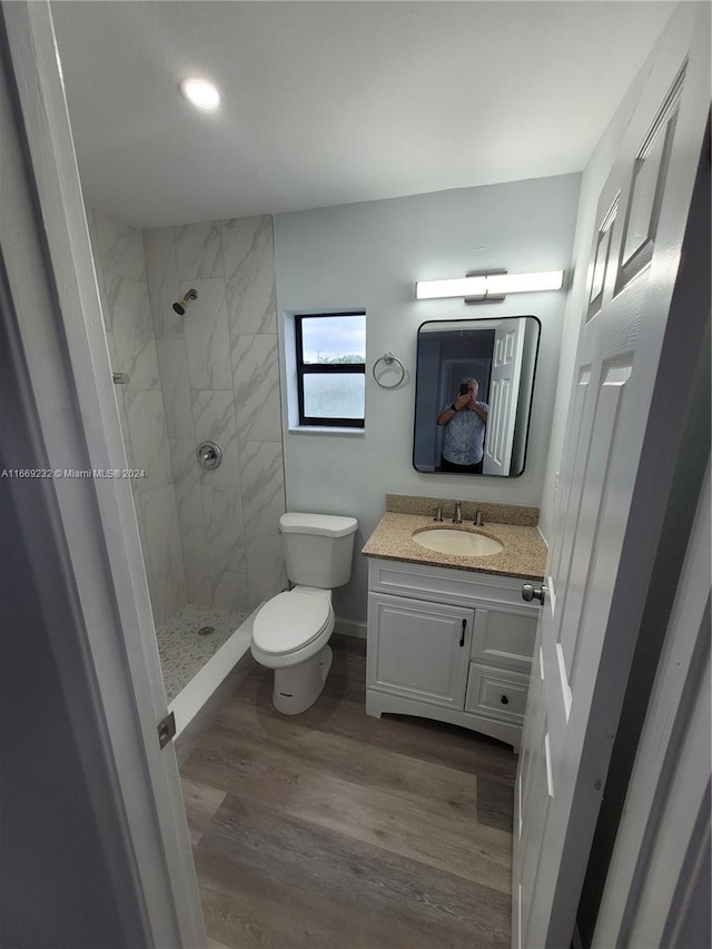 bathroom with a tile shower, vanity, wood-type flooring, and toilet