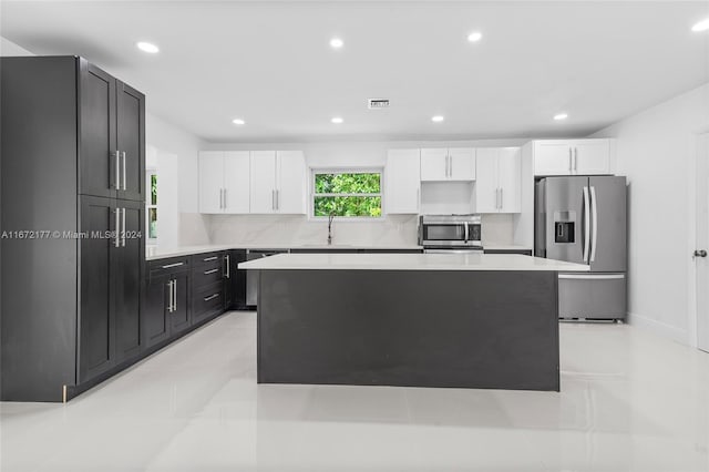 kitchen with sink, decorative backsplash, appliances with stainless steel finishes, a kitchen island, and white cabinetry