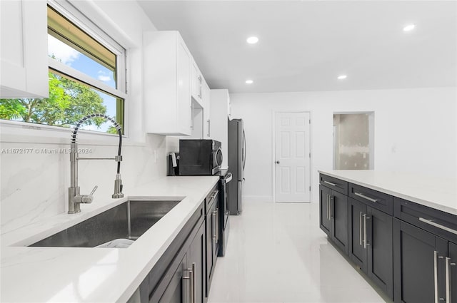 kitchen with sink, decorative backsplash, light stone counters, white cabinetry, and stainless steel refrigerator