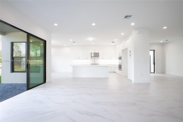 interior space featuring white cabinets, an island with sink, and double oven