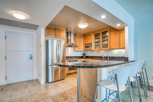 kitchen with kitchen peninsula, a breakfast bar, stainless steel appliances, and wall chimney exhaust hood