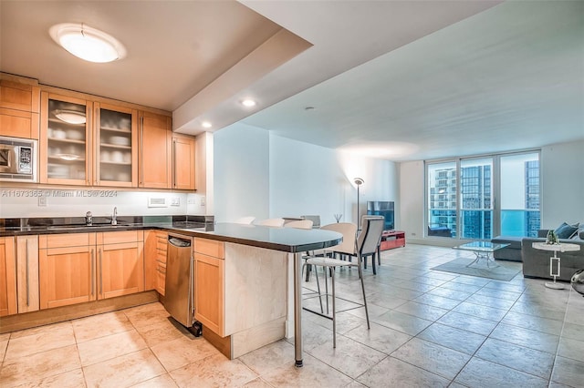 kitchen with stainless steel microwave, sink, light brown cabinets, kitchen peninsula, and a breakfast bar