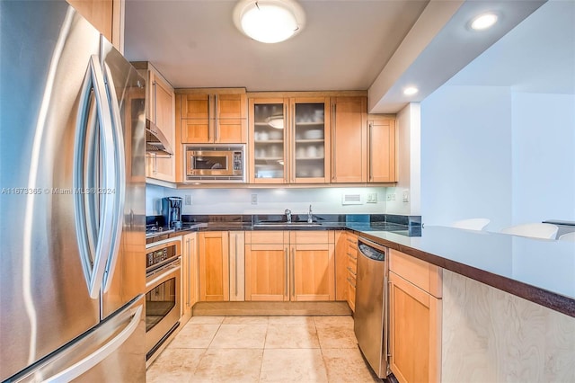 kitchen with sink, range hood, light brown cabinetry, light tile patterned floors, and appliances with stainless steel finishes