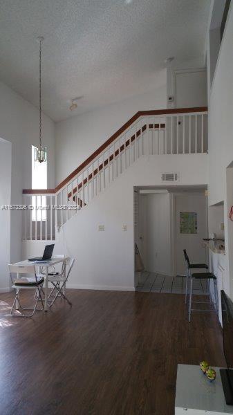 3204 Glenmoor Dr Unit 3204, West Palm Beach, FL 33409 - unfurnished living room featuring high vaulted ceiling, wood finished floors, stairs, a textured ceiling, and baseboards