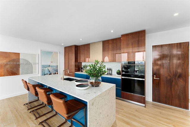 kitchen featuring backsplash, a breakfast bar area, a kitchen island with sink, and light wood-type flooring