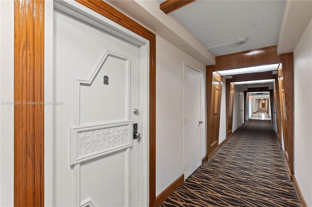 hall featuring wood walls, a textured ceiling, and dark colored carpet