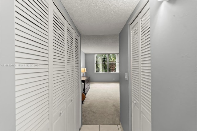 corridor with a textured ceiling and light colored carpet