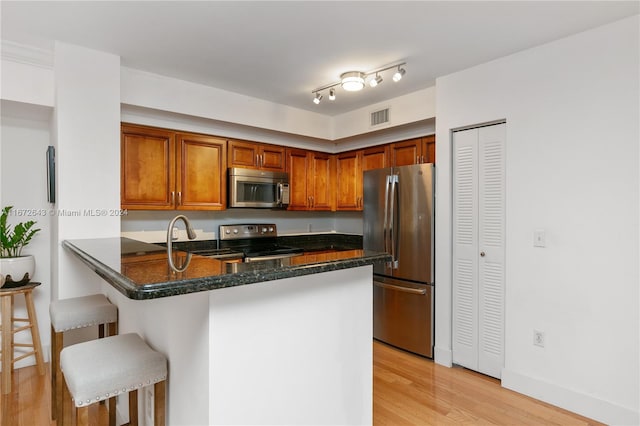 kitchen with kitchen peninsula, a breakfast bar area, stainless steel appliances, light wood-type flooring, and dark stone counters