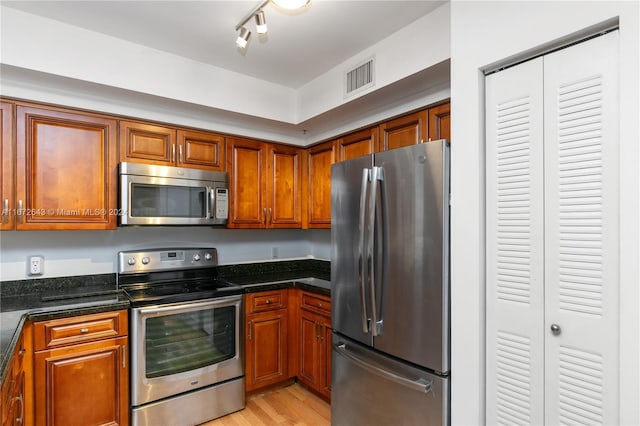 kitchen with dark stone counters, stainless steel appliances, light wood-type flooring, and rail lighting