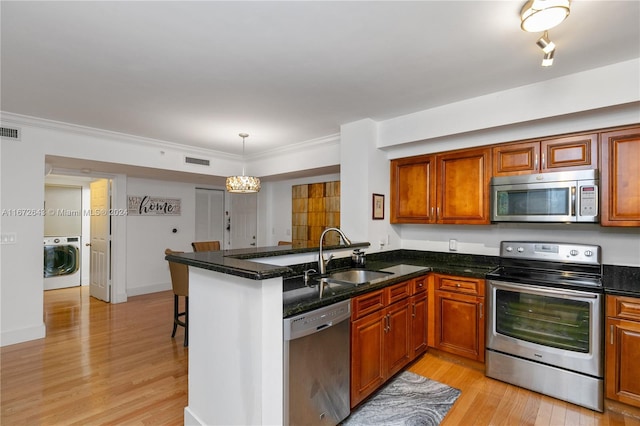 kitchen with appliances with stainless steel finishes, kitchen peninsula, light wood-type flooring, washer / dryer, and sink