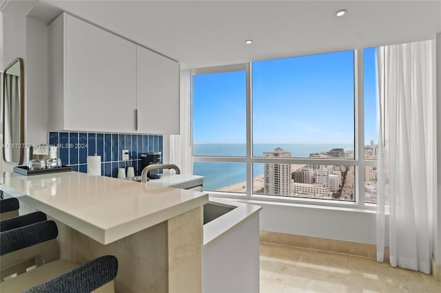 kitchen with white cabinetry, a water view, tasteful backsplash, and kitchen peninsula