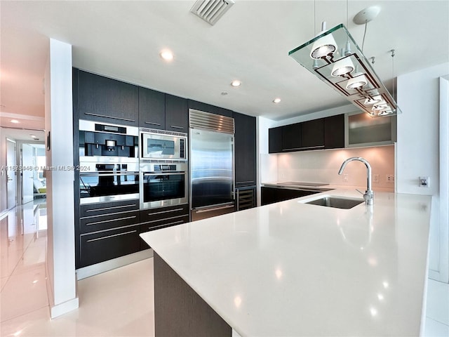 kitchen featuring kitchen peninsula, sink, light tile patterned floors, built in appliances, and hanging light fixtures