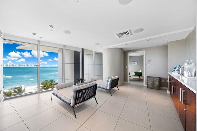 living room with floor to ceiling windows, a water view, light tile patterned floors, and a view of the beach