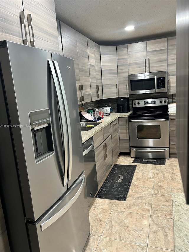 kitchen with tile walls, light stone counters, a textured ceiling, and appliances with stainless steel finishes