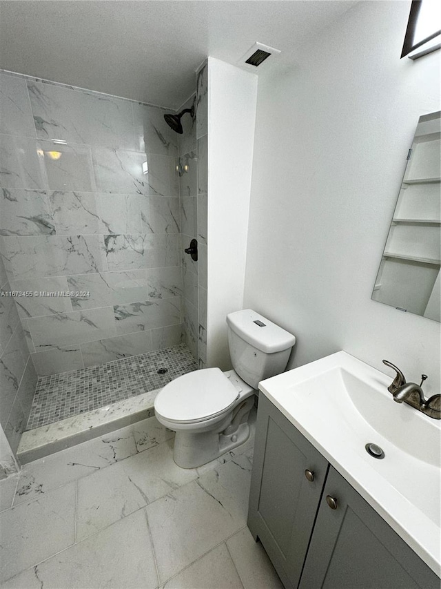 bathroom featuring vanity, a tile shower, and toilet