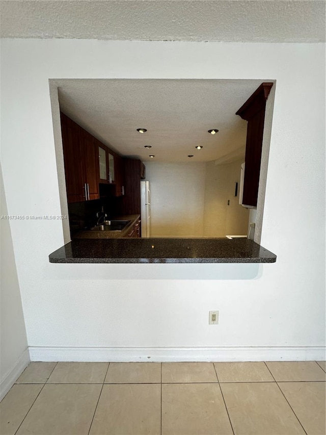 kitchen with kitchen peninsula, light tile patterned floors, a textured ceiling, fridge, and sink