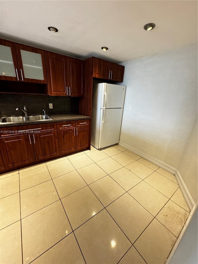 kitchen with light tile patterned floors, white refrigerator, sink, and decorative backsplash