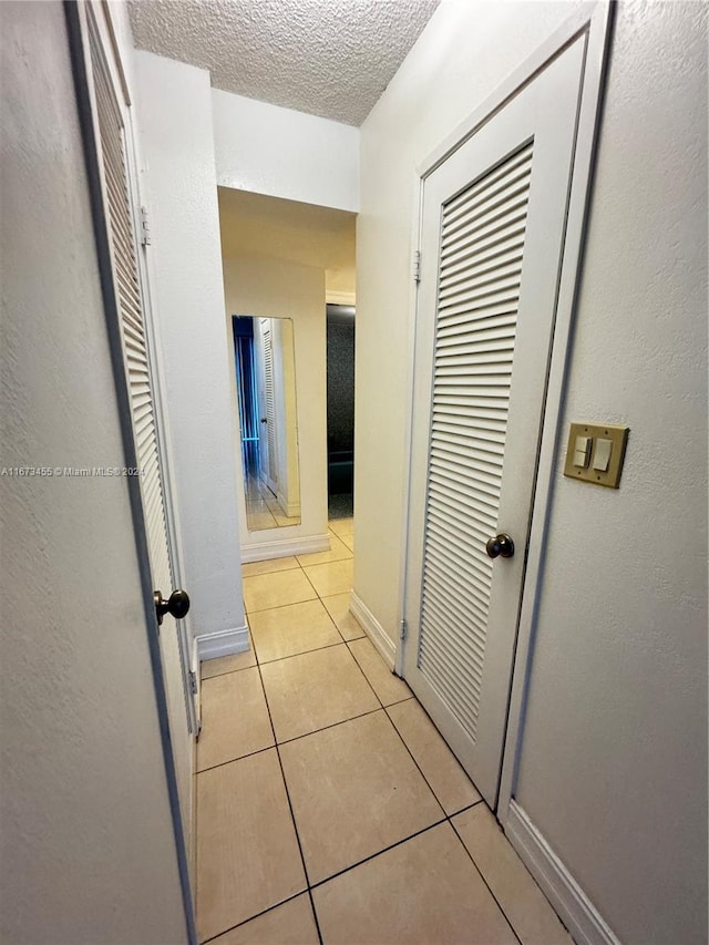 hallway with a textured ceiling and light tile patterned floors