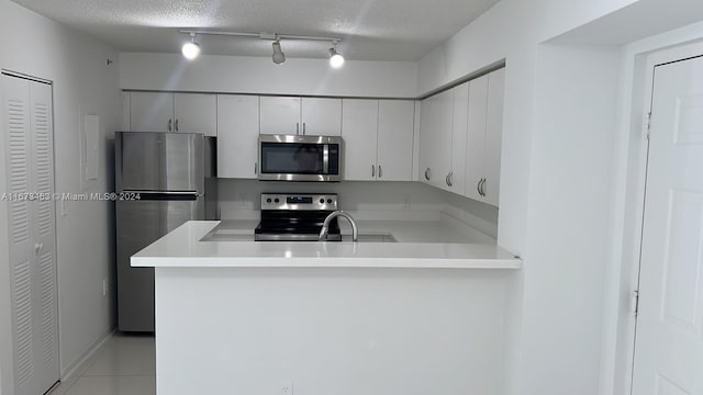 kitchen with track lighting, a textured ceiling, appliances with stainless steel finishes, and kitchen peninsula