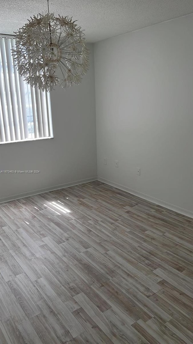 empty room featuring a textured ceiling, hardwood / wood-style floors, and a chandelier