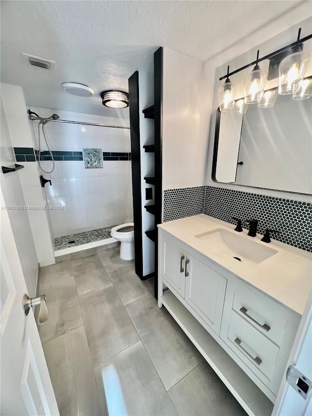 bathroom featuring vanity, toilet, a textured ceiling, a tile shower, and tile patterned flooring