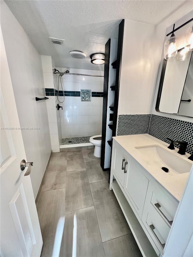 bathroom with vanity, toilet, a textured ceiling, and tiled shower