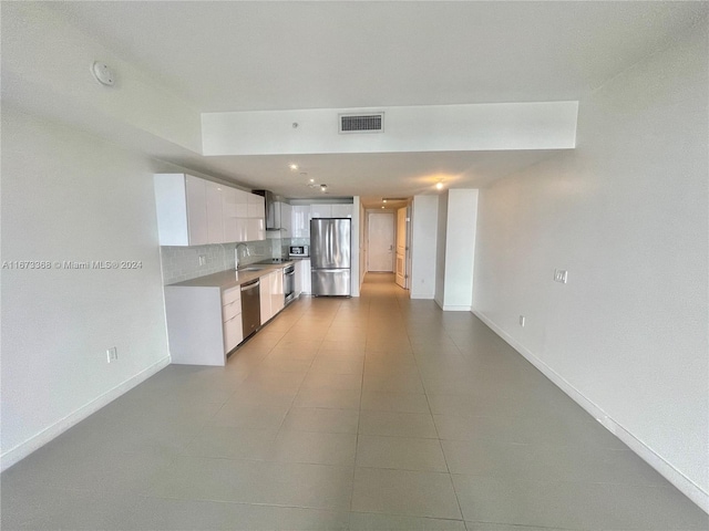 kitchen with sink, white cabinets, backsplash, appliances with stainless steel finishes, and light tile patterned floors