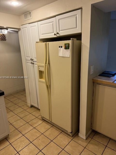 kitchen with white fridge with ice dispenser, light tile patterned floors, and white cabinetry