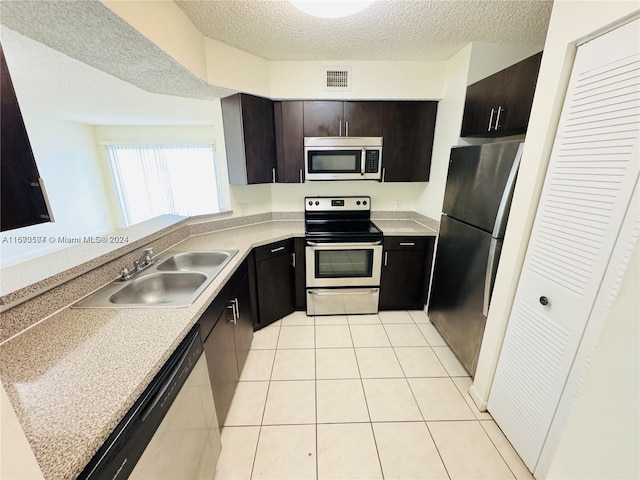 kitchen featuring light tile patterned floors, sink, dark brown cabinets, a textured ceiling, and appliances with stainless steel finishes