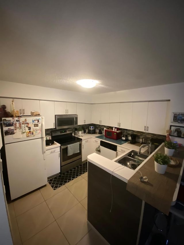 kitchen featuring light tile patterned flooring, sink, white cabinetry, kitchen peninsula, and appliances with stainless steel finishes