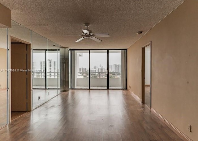 unfurnished room with a textured ceiling, a wall of windows, hardwood / wood-style floors, and ceiling fan