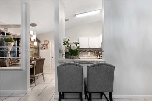 interior space with white cabinets, backsplash, decorative light fixtures, lofted ceiling, and light tile patterned floors