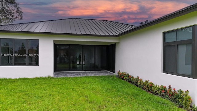 back house at dusk featuring a sunroom and a lawn