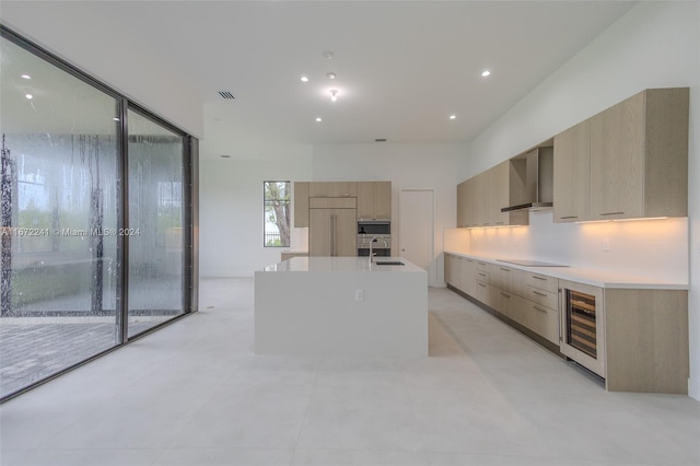 kitchen with sink, beverage cooler, wall chimney exhaust hood, a center island with sink, and light brown cabinetry