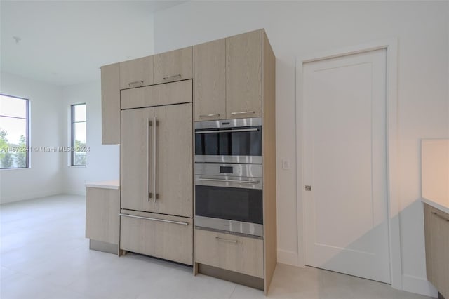 kitchen with paneled refrigerator, light brown cabinetry, and stainless steel double oven