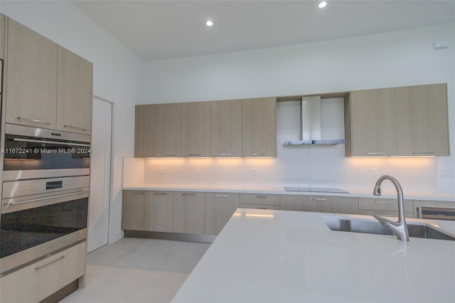 kitchen featuring light brown cabinets, black cooktop, wall chimney range hood, and sink